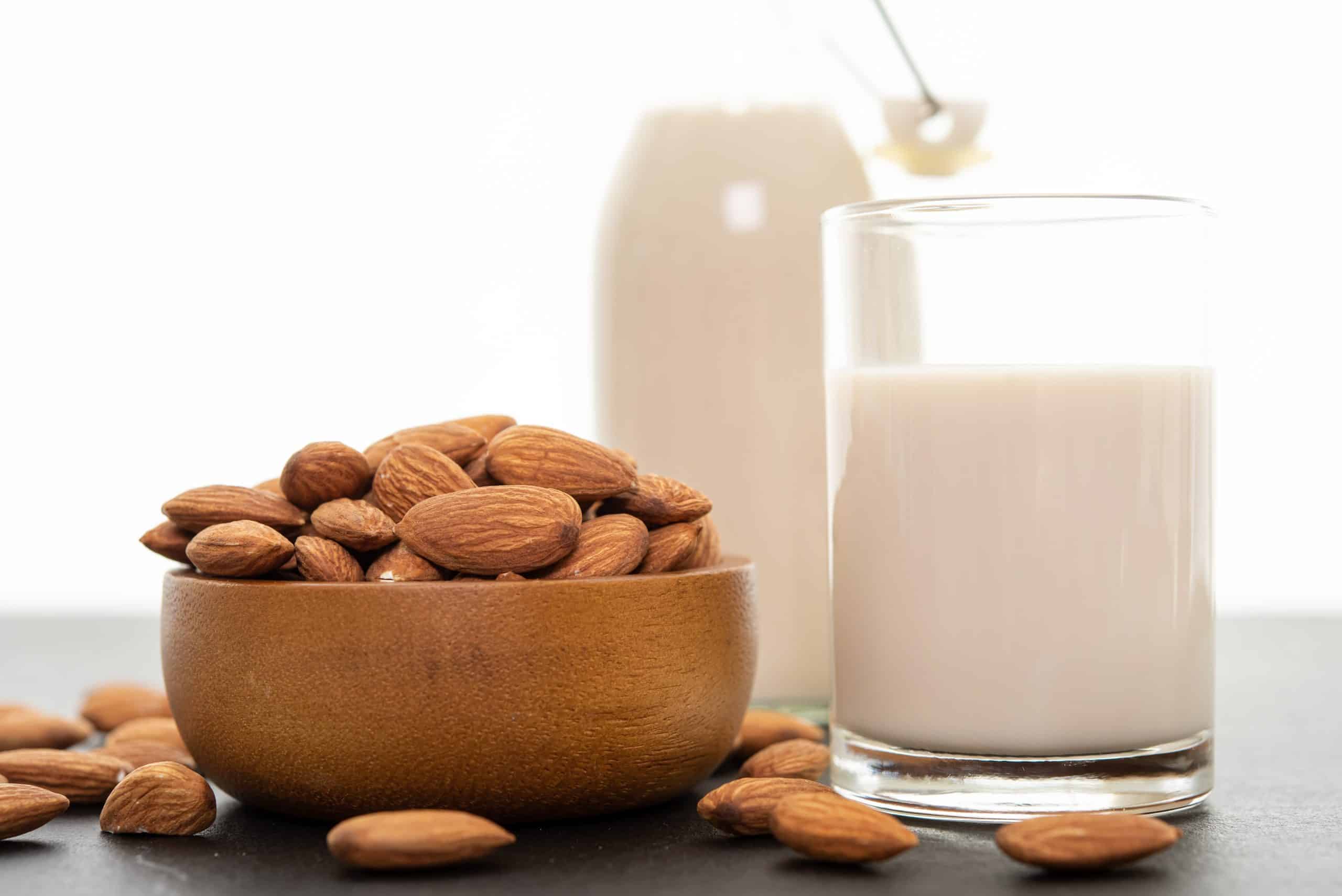 Almond milk with almond in a wooden bowl on black background. (s